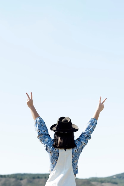 Foto parte trasera de un signo de victoria de una mujer con sombrero y fondo de cielo azul.