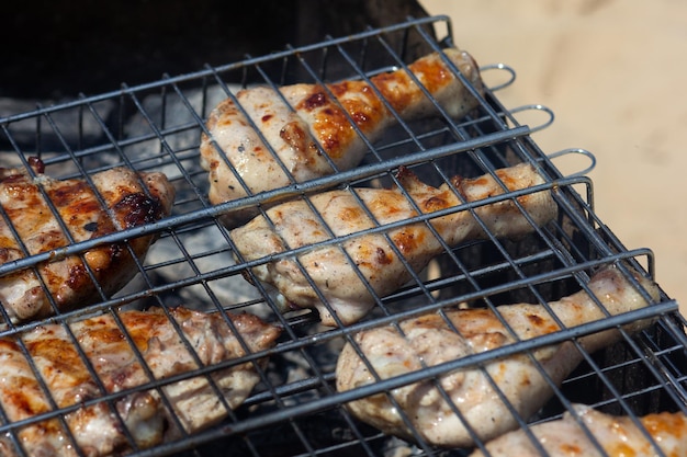 Partes grelhadas de frango na grelha cozinhando em carvão fumegante ao ar livre