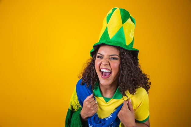 Partidario de Brasil. Ventilador brasileño de mujer de pelo rizado celebrando en fútbol, partido de fútbol sobre fondo amarillo. Colores de Brasil.