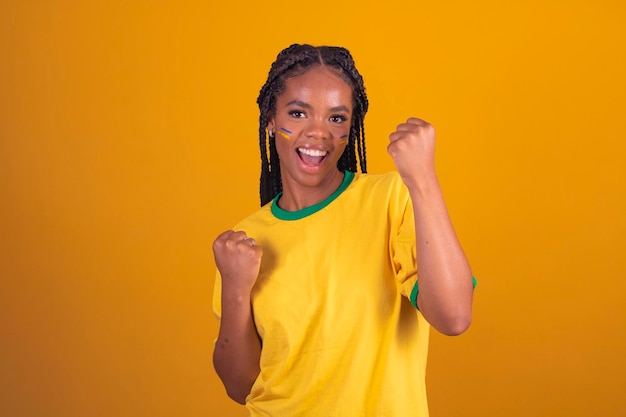 Partidario brasileño Fanático de la mujer brasileña celebrando el fútbol o el partido de fútbol con fondo amarillo Colores de Brasil