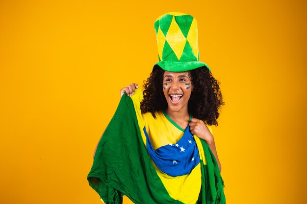 Partidario brasileño. Ventilador de mujer brasileña celebrando en fútbol o partido de fútbol sobre fondo amarillo. Colores de Brasil.