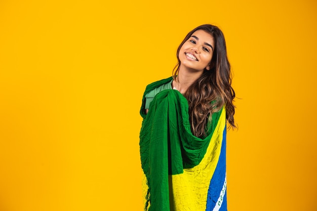 Partidario brasileño. Ventilador de mujer brasileña celebrando en fútbol o partido de fútbol sobre fondo amarillo. Colores de Brasil.