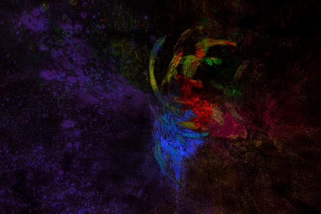 Partikel von Holi-Farben gemischt mit der Hand auf schwarzem Hintergrund