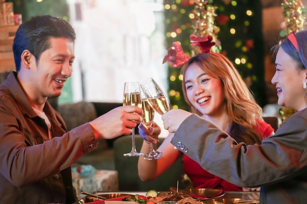 Party asiatischer Freunde, die Weihnachtsgetränke genießen und feiern. Nahaufnahme von klirrenden Gläsern Champagner mit Beleuchtung und Glanz. Glück Menschen Heiligabend feiern Abendessen mit Essen.