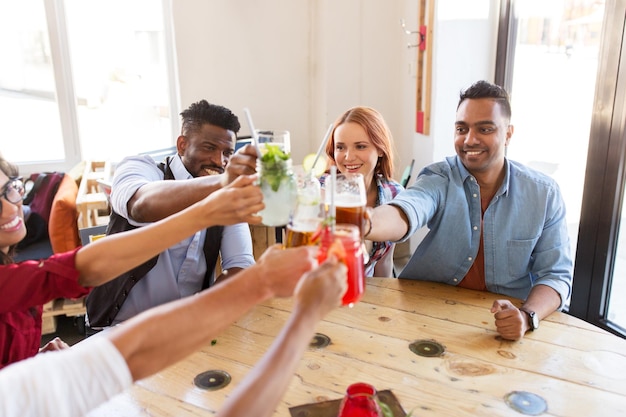 Party-, Feier- und People-Konzept – eine Gruppe glücklicher internationaler Freunde, die am Restauranttisch Getränkegläser anstoßen