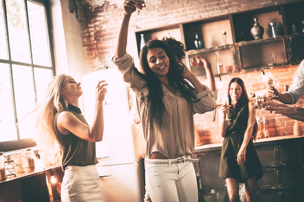 Party ist alles, was sie brauchen. Fröhliche junge Leute tanzen und trinken, während sie die Party in der Küche genießen