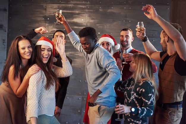 Party mit Freunden. Sie lieben Weihnachten. Gruppe fröhlicher junger Leute, die Wunderkerzen und Champagnerflöten tragen, die in der Neujahrsparty tanzen und glücklich schauen. Konzepte über Zusammengehörigkeit Lebensstil