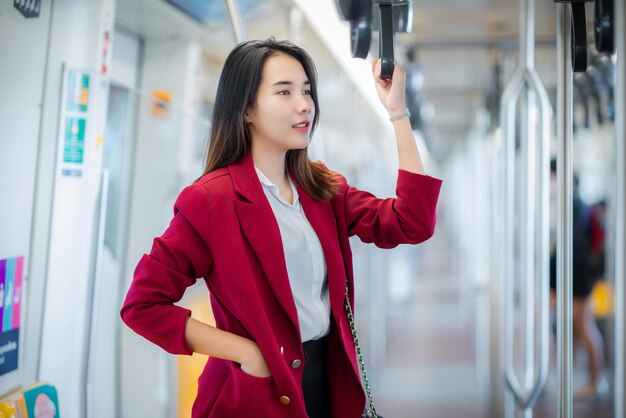 Pasajera asiática en uniforme de empleada de oficina de pie en el tren BTS mientras viaja en Bangkok