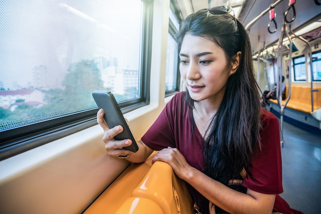 Pasajero asiático con traje casual usando el teléfono móvil inteligente en los rieles BTS Skytrain o MRT