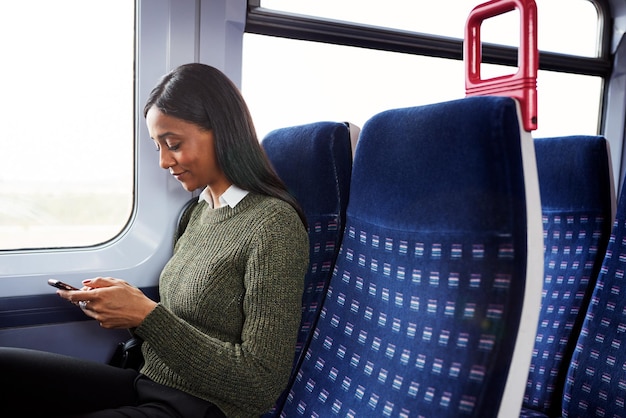 Pasajero femenino sentado en el tren mirando el teléfono móvil