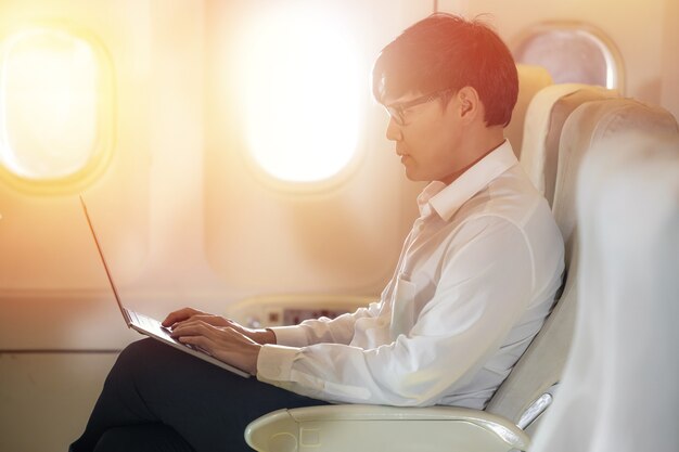 Pasajero masculino asiático en avión lee noticias de las redes a través de una computadora portátil y wifi a bordo
