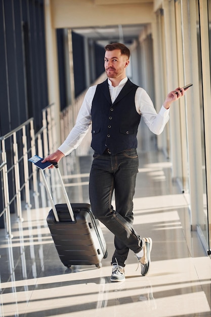 Foto pasajero masculino con ropa elegante y formal está en la sala del aeropuerto con equipaje, boletos y teléfono.