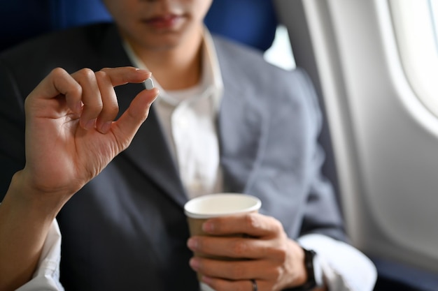 Un pasajero masculino sosteniendo una taza de agua y pastillas para el mareo por movimiento