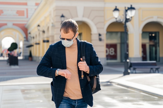 El pasajero masculino verifica el tiempo de guardia espera la llegada del autobús lleva una mochila usa una máscara médica desechable protectora protege de los virus Covid19 miedo al riesgo de infección viaja solo