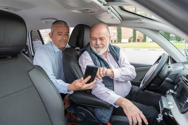 Pasajero de mediana edad en el asiento trasero mostrando su teléfono inteligente a un conductor mayor concepto de taxi de transporte y tecnología