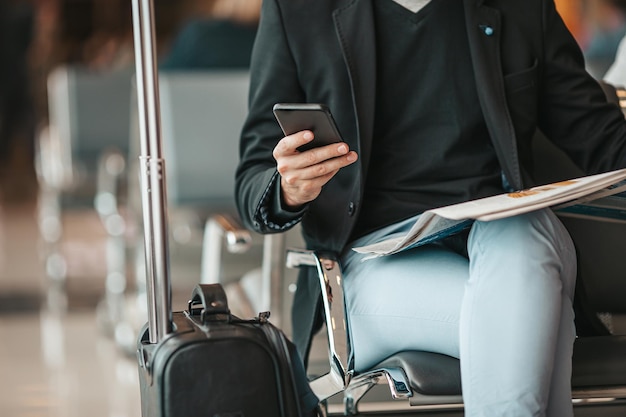 Pasajero en un salón del aeropuerto esperando el avión de vuelo joven con teléfono inteligente en espera del aeropuerto