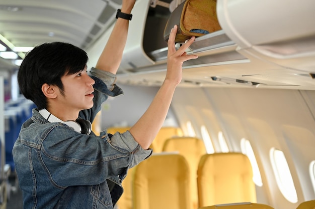 Pasajero de viajero masculino asiático poniendo su equipaje de mano en el casillero superior antes del despegue