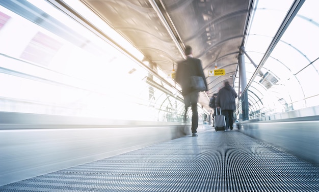 Pasajeros borrosos en movimiento en un skywalk en un aeropuerto moderno. ideal para sitios web y diseños de revistas.