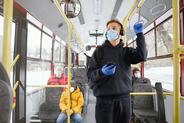 Pasajeros que se van a casa en transporte público de pie sentados con máscaras y guantes médicos