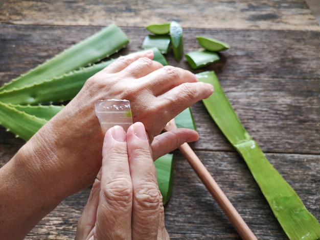 Pasando aloe vera en la mano y rodajas de hojas sobre fondo rústico de madera.