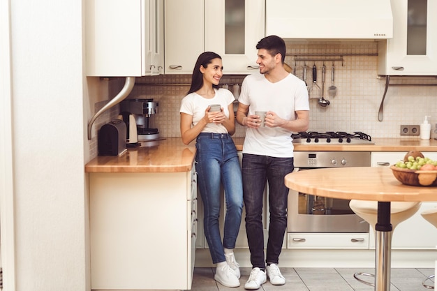 Pasando tiempo juntos. Retrato de cuerpo entero de lindo joven y mujer tomando café de pie en la cocina moderna