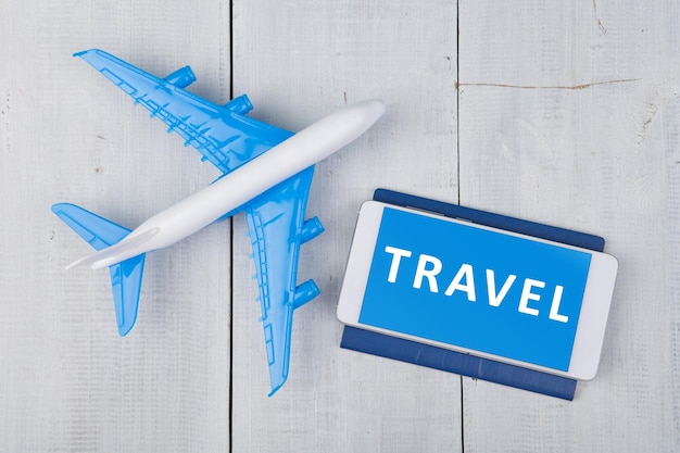 Pasaporte de avión y teléfono inteligente con palabra VIAJE en mesa de madera blanca