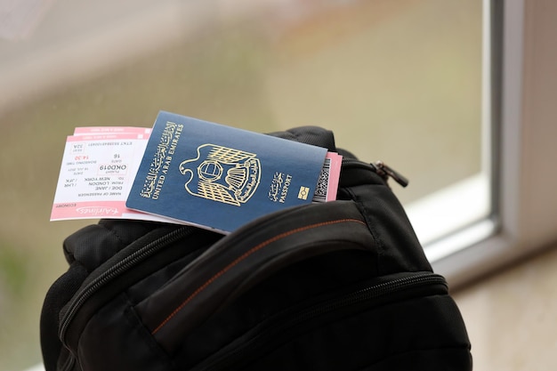 Pasaporte azul de los Emiratos Árabes Unidos con billetes de avión en una mochila turística