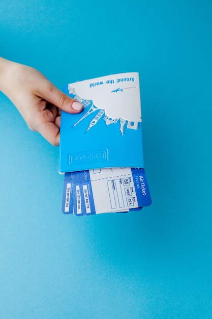 Foto pasaporte y boleto aéreo en mano de mujer sobre un fondo azul.