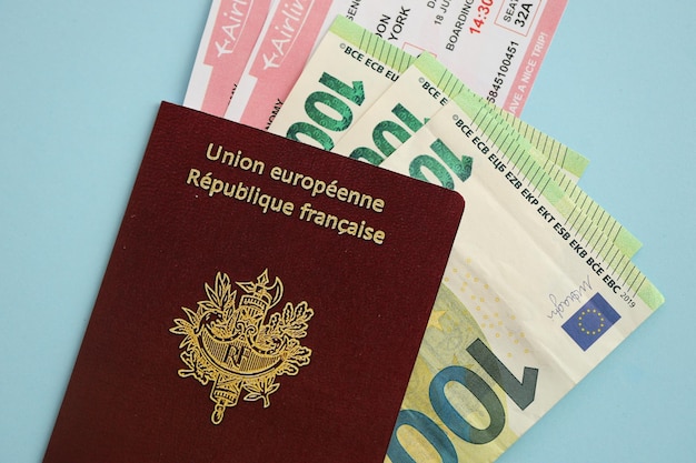 Pasaporte francés y dinero en euros con billetes de avión sobre fondo azul