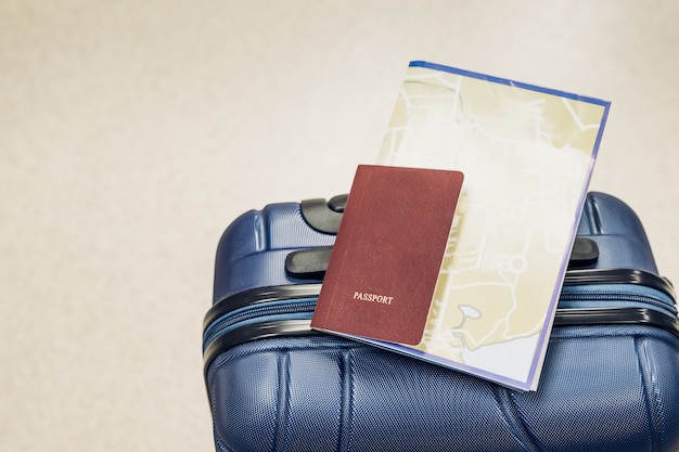 Foto el pasaporte y el mapa cercanos ponen en la maleta azul en el aeropuerto, concepto de las vacaciones del viaje