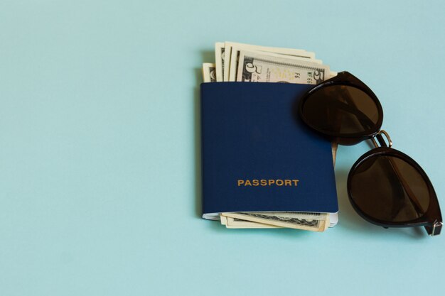 Pasaporte con moneda y gafas de sol sobre fondo pastel