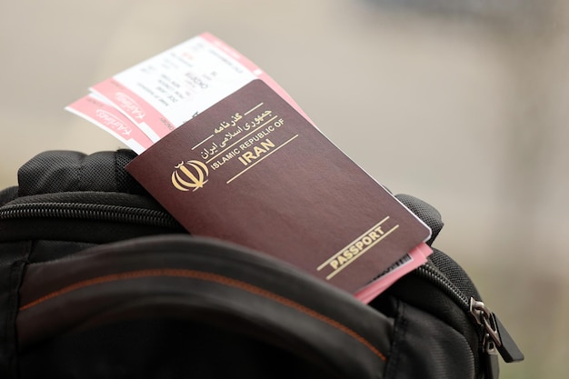 Pasaporte rojo de la República Islámica de Irán con billetes de avión en una mochila turística