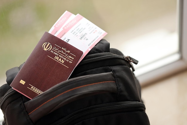 Pasaporte rojo de la República Islámica de Irán con billetes de avión en una mochila turística