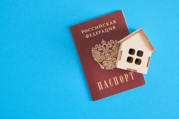 Pasaporte ruso y casa de juguete de madera sobre un fondo azul el concepto de comprar bienes raíces