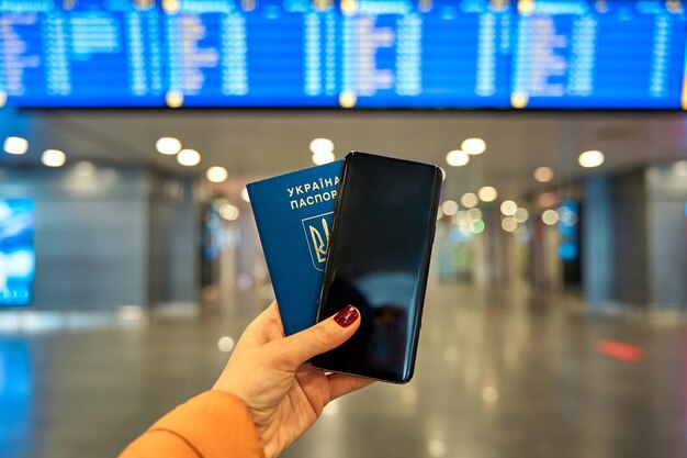 Pasaporte y teléfono en mano en el panel de información del aeropuerto.