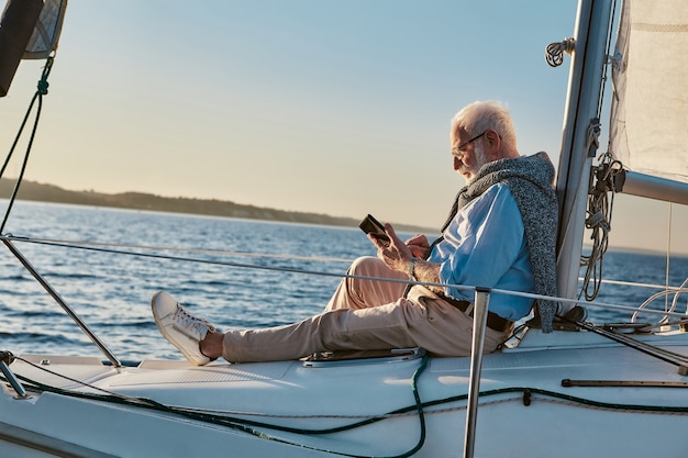 Pasar algún tiempo solo vista lateral de un hombre mayor relajado sentado en el costado del velero o yate