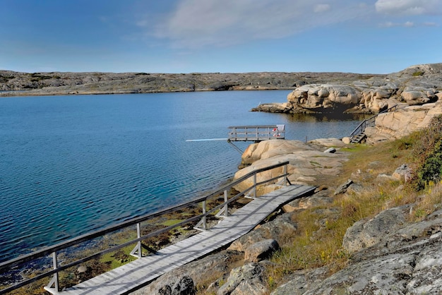 Pasarela de madera a lo largo de la costa rocosa y un trampolín en una playa en Suecia xA