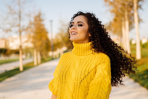 En la pasarela del parque con un suéter amarillo brillante se encuentra con el pelo revoloteando una hermosa sonrisa