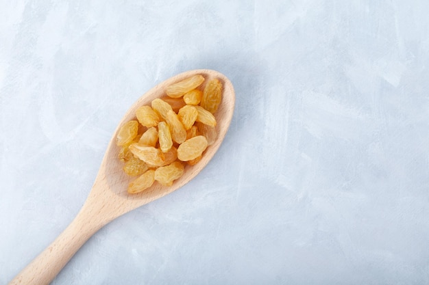 Pasas amarillas en cuchara de madera sobre fondo gris Fruta de uva deshidratada seca