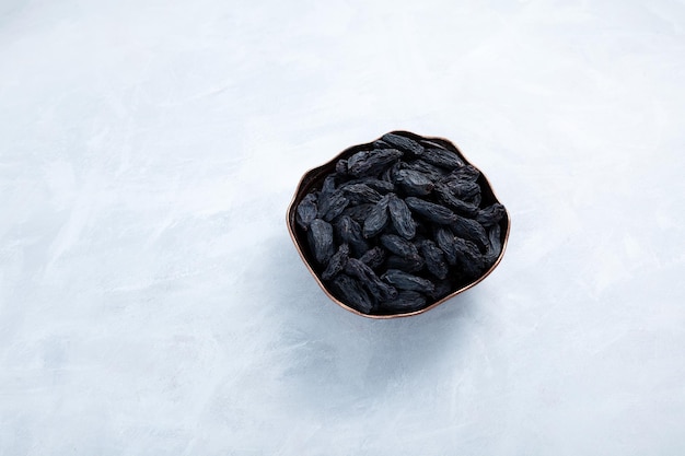 Pasas negras sin semillas en un tazón de metal sobre fondo gris, vista superior. Fruta de uva deshidratada seca.