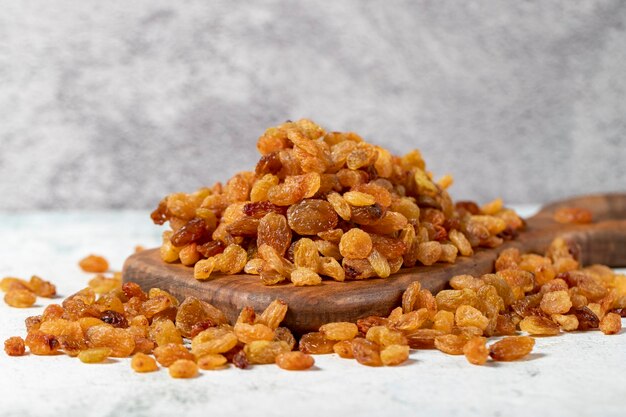 Pasas sobre fondo de piedra Una pila orgánica de pasas amarillas en un tablero de madera para servir nueces sanas secas de cerca