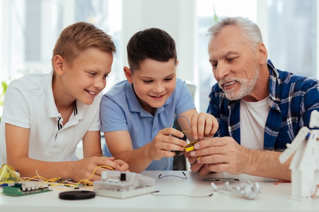 Pasatiempo agradable. niños inteligentes alegres sentados junto con su abuelo mientras se divierten