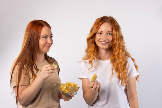 El pasatiempo de las amigas pelirrojas mujeres comen papas fritas en una pared blanca