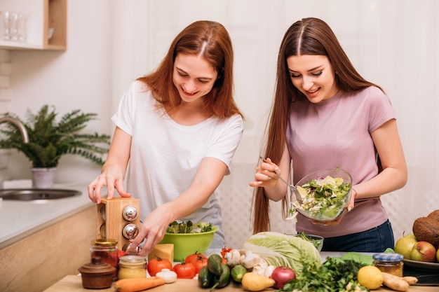 Pasatiempo de cocina. Comidas orgánicas. Estilo de vida saludable. Dos hembras jóvenes sonriendo haciendo ensalada verde.