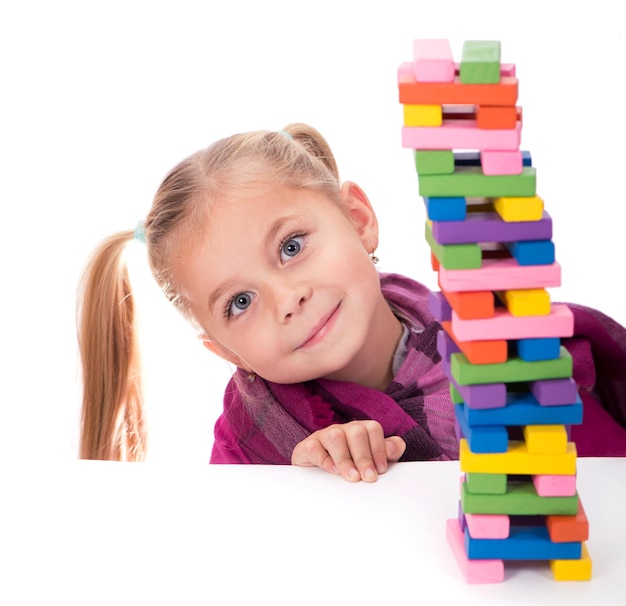 Los pasatiempos de los niños, la creatividad, una niña con un vestido azul jugando con el juego de madera jenga sobre fondo blanco.