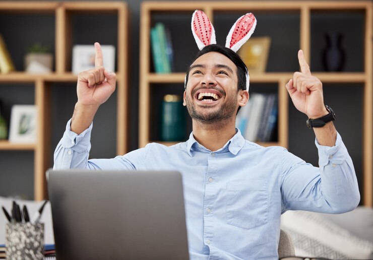 Páscoa de orelhas de coelho e celebração pelo homem de negócios animado feliz e ganhando em um escritório com sucesso Coelho vencedor e funcionário ou pessoa com conquista de vitória e usando um laptop para obter lucro