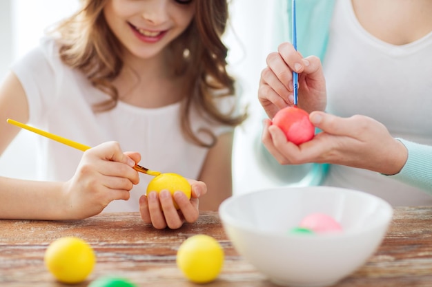 Páscoa, família, férias e conceito de criança - close-up de menina e mãe colorindo ovos para a páscoa