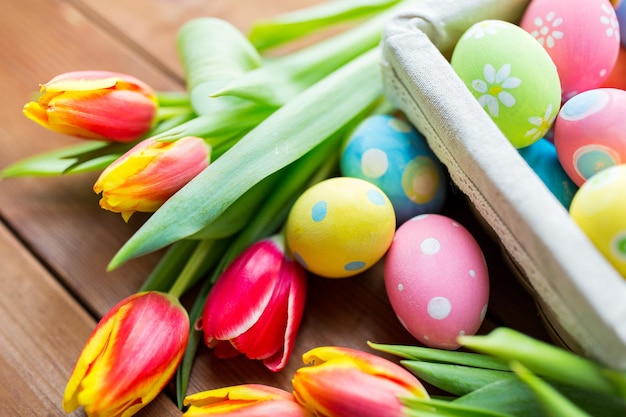 páscoa, feriados, tradição e conceito de objeto - close-up de ovos de páscoa coloridos na cesta e flores de tulipa