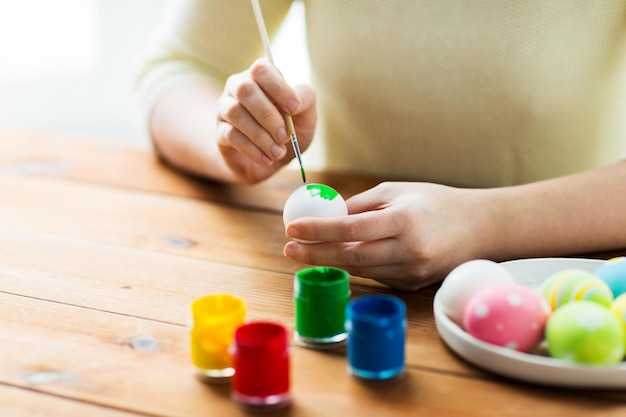 páscoa, feriados, tradição e conceito de pessoas - close-up de mãos de mulher colorindo ovos de páscoa com cores e pincel