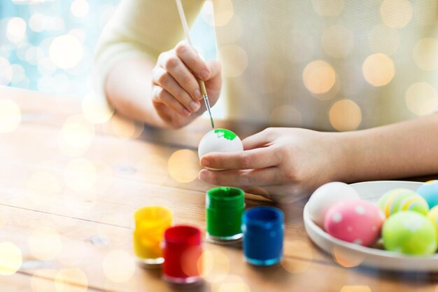 páscoa, feriados, tradição e conceito de pessoas - close-up de mãos de mulher colorindo ovos de páscoa com cores e pincel